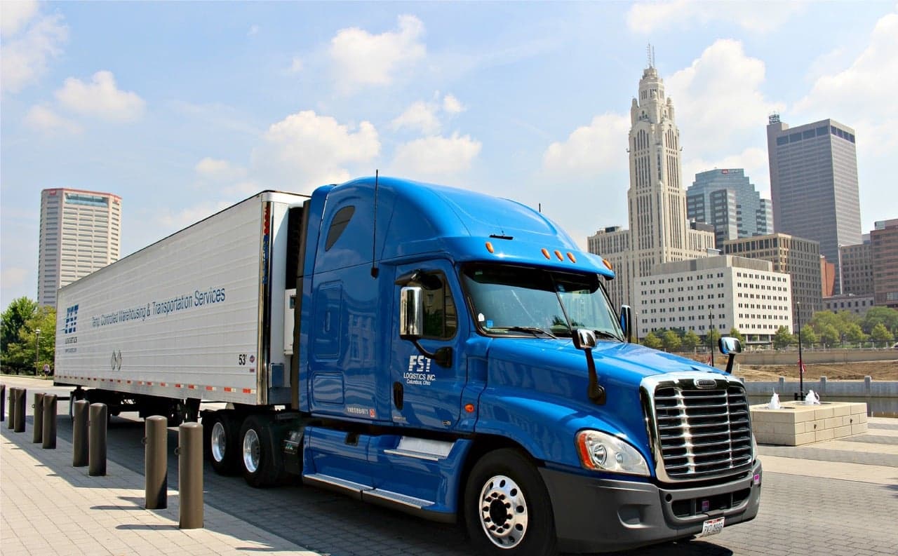 Blue FST Logistics semi-truck with trailer parked in downtown Columbus cityscape