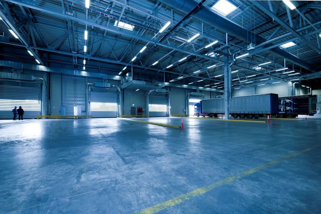 Large industrial warehouse interior with truck, loading docks, and fluorescent lighting