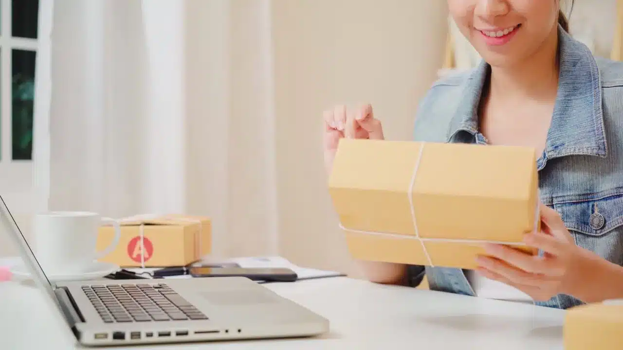 Woman managing warehouse shipments with laptop and packages for WMS inventory control
