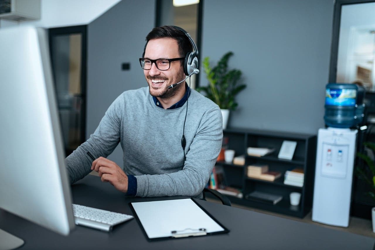 Smiling man with headset and glasses working at computer in modern office