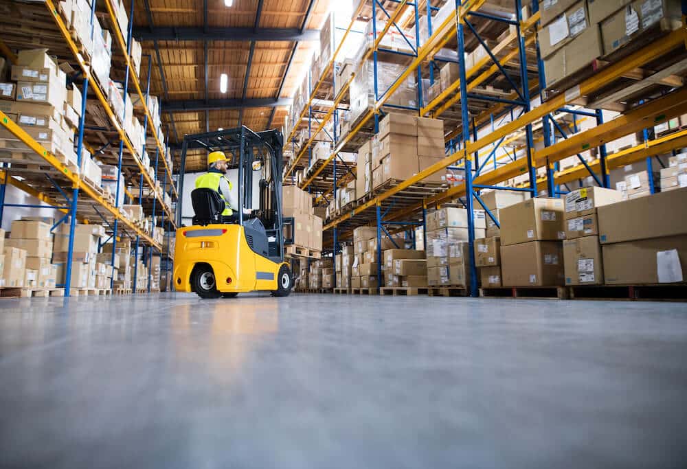 Warehouse worker operating yellow forklift among tall storage shelves with boxes