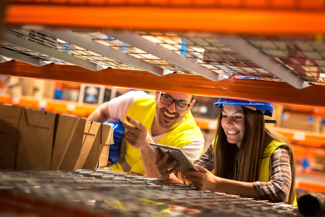 Warehouse workers in safety vests counting inventory boxes on distribution center shelves