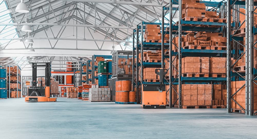 Large concrete warehouse with tall shelving units storing pallets and orange forklifts