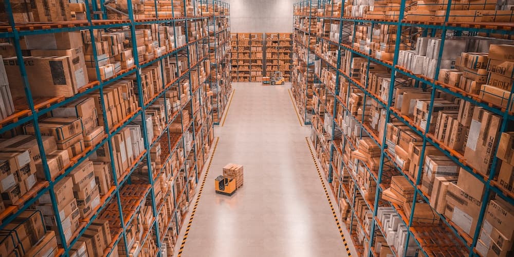 Large warehouse interior with stacked boxes on shelving and yellow forklift in aisle