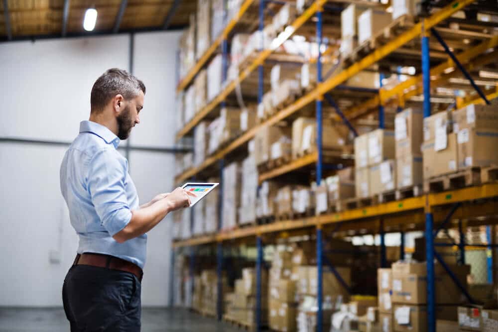 Male warehouse manager using tablet to track inventory in distribution center