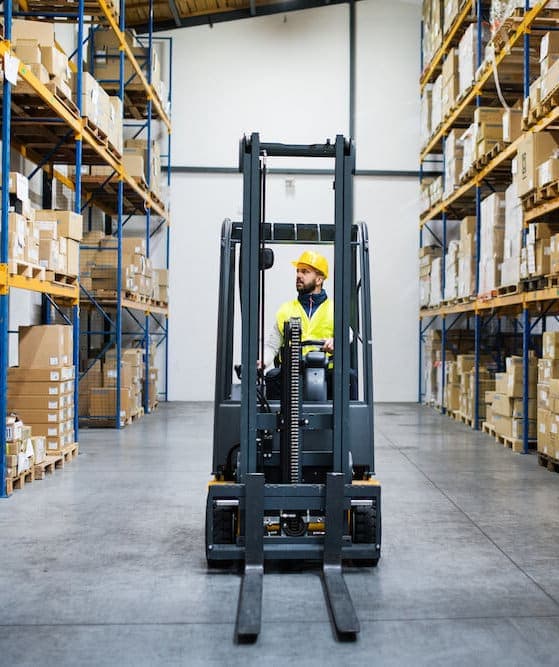 Warehouse worker in yellow safety vest operating forklift in industrial storage facility