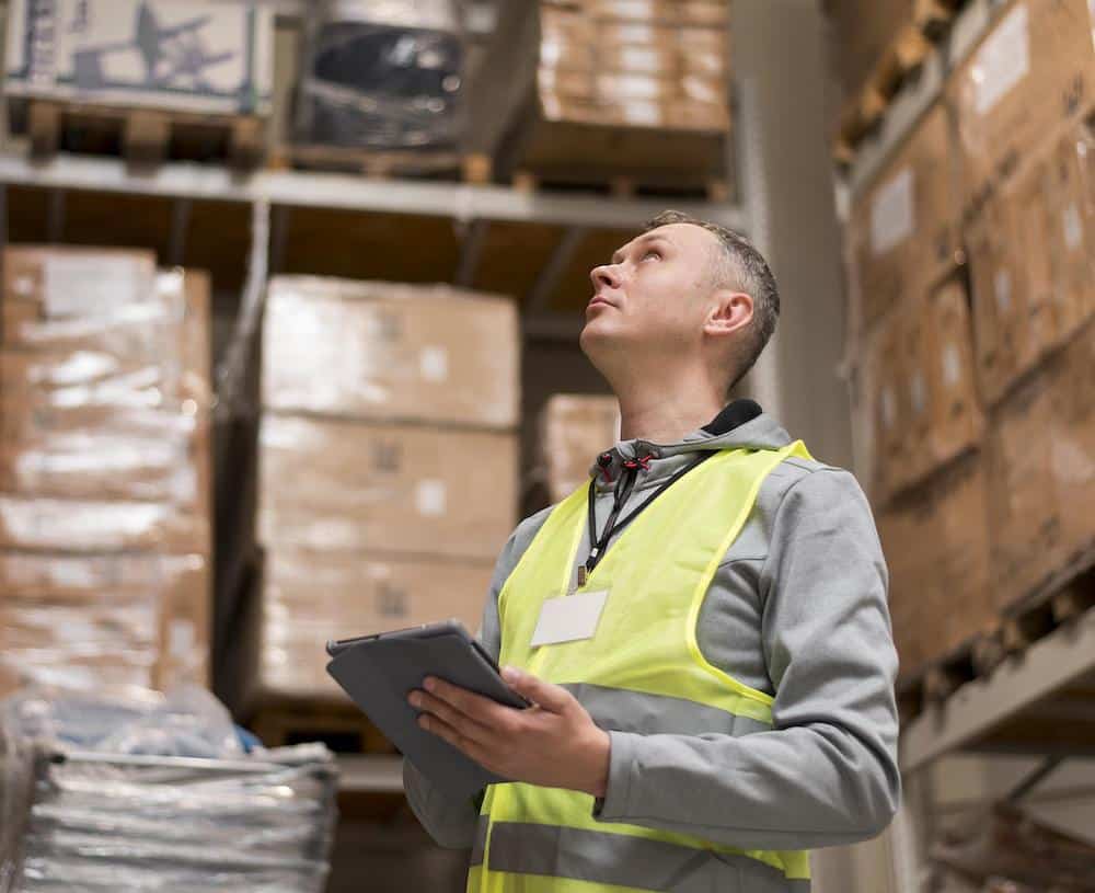 Professional warehouse manager in suit and tie holding tablet among storage shelves