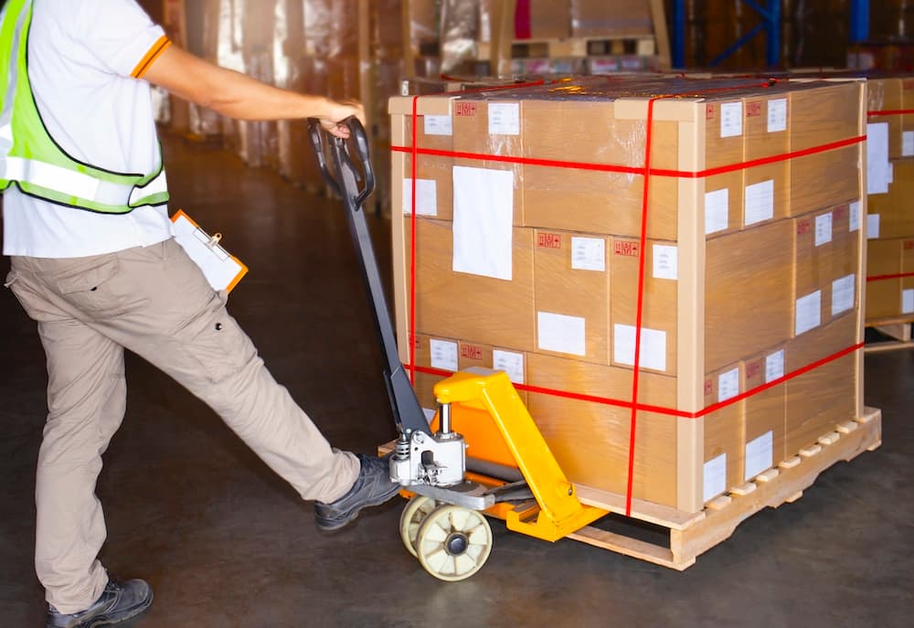 Warehouse worker using pallet jack to move boxes in shipping facility