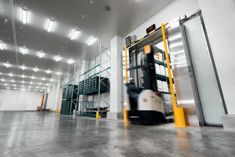 Worker operating stand-on stacker truck moving pallets in modern warehouse facility