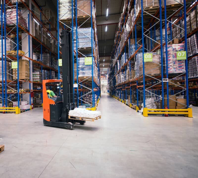 Large warehouse interior with orange forklift, pallet racking systems and inventory storage