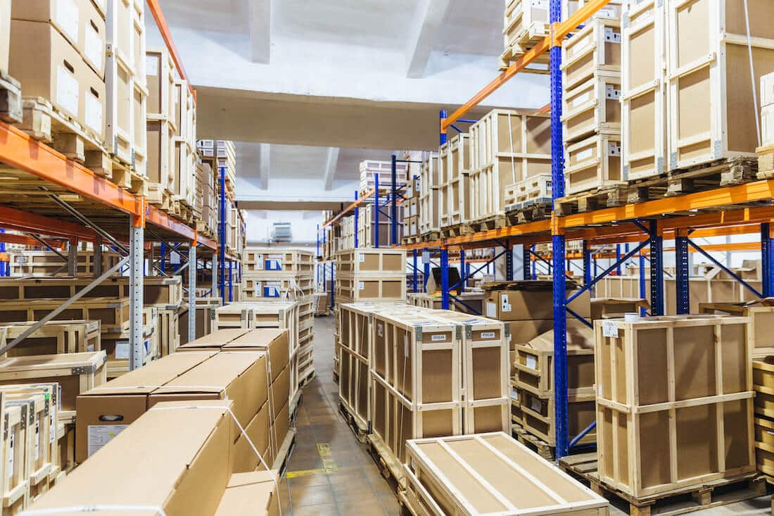 Empty warehouse interior with tall shelving units storing wooden crates and cardboard boxes