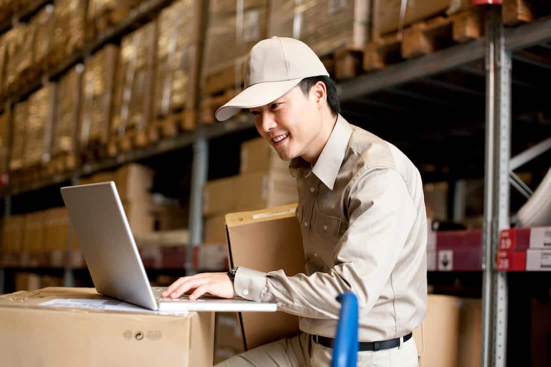 Male warehouse worker in uniform using laptop computer in distribution center