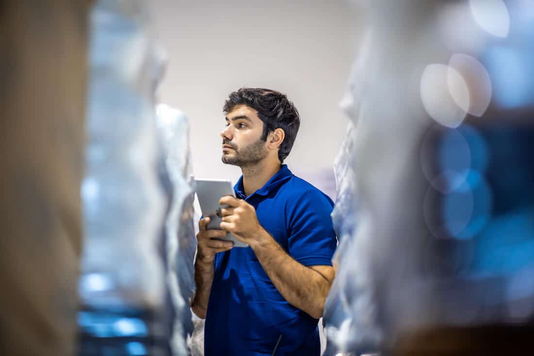 Male warehouse worker in blue shirt checking smartphone in storage facility