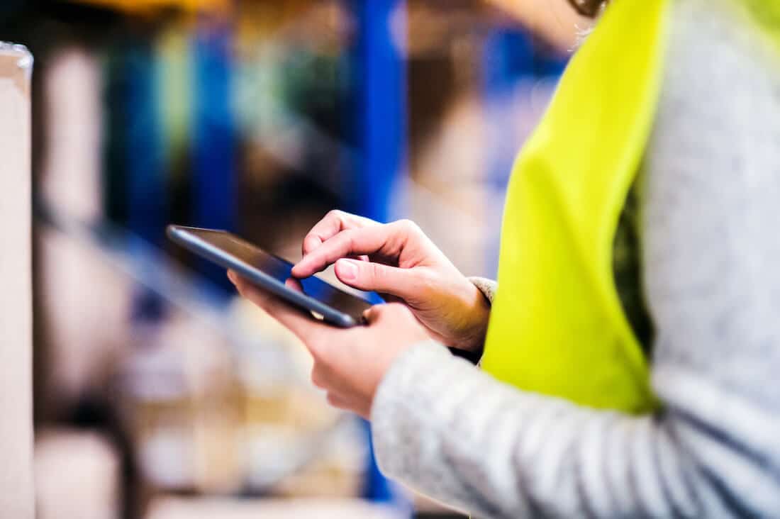 Female warehouse worker in yellow vest using tablet for inventory management