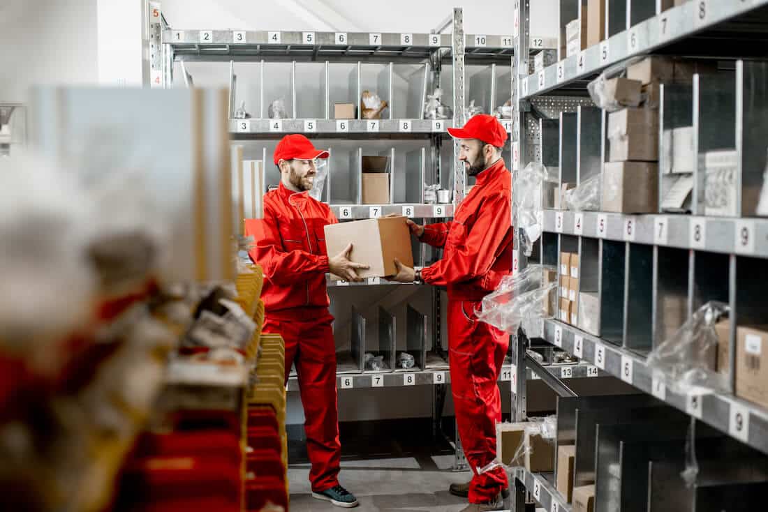Two warehouse workers in red uniforms organizing inventory on metal shelving
