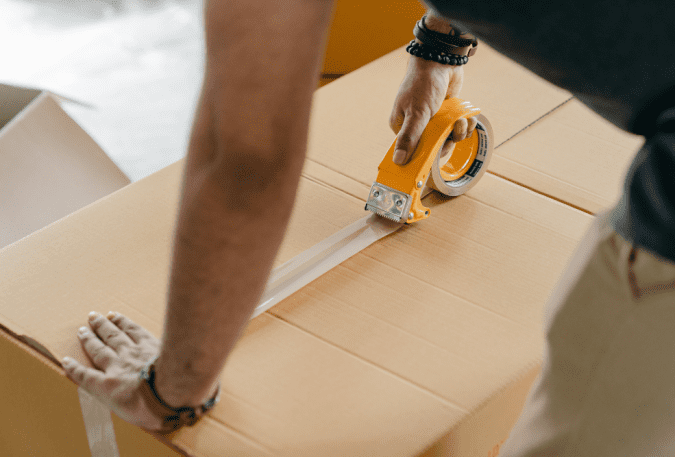 Person sealing cardboard boxes with packing tape for shipping or moving