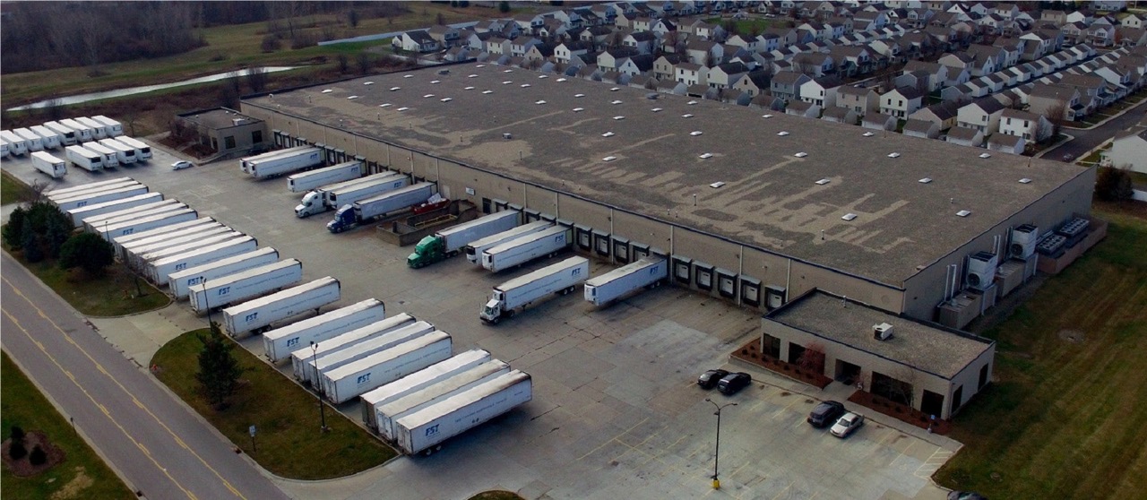 Large FST warehouse facility with loading docks and parked delivery trailers from aerial view