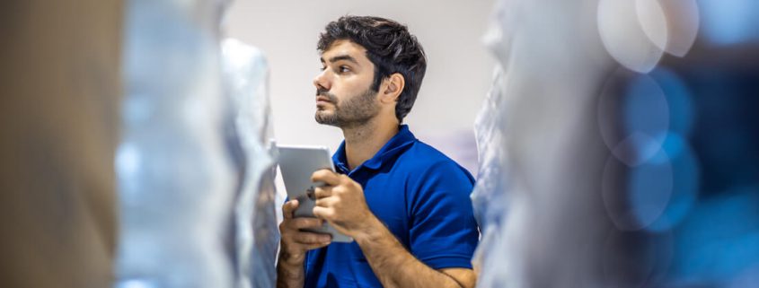 Male warehouse worker in blue shirt checking smartphone in storage facility