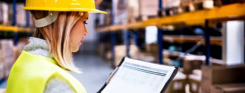 Female warehouse worker in yellow hard hat using digital tablet for inventory management