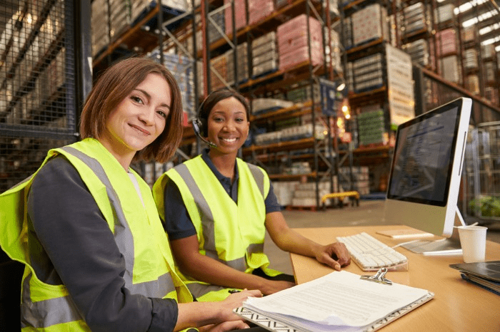 two warehouse workers in front of a computer screen, one with a headset