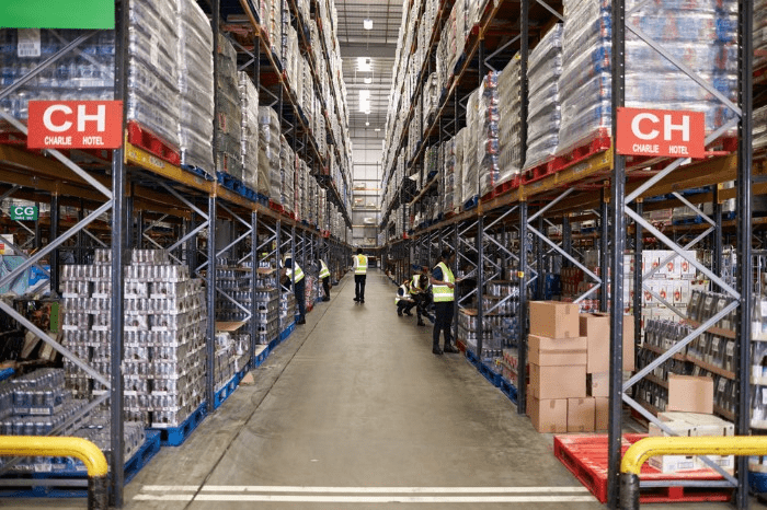 workers checking inventory in a food and beverage warehouse, aisles marked with row labels