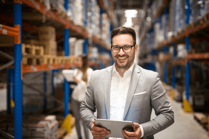man in suite in a warehouse holding a tablet and smiling