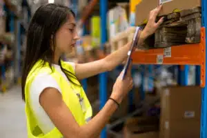 warehouse worker doing a cycle count of inventory, holding a tablet while looking at a box