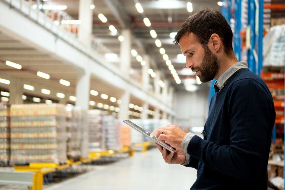 man looking at a tablet pallets in a warehouse in the background