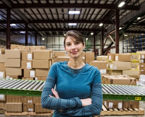 a-caucasian-female-warehouse-worker-in-a-distribution warehouse in front of a conveyor