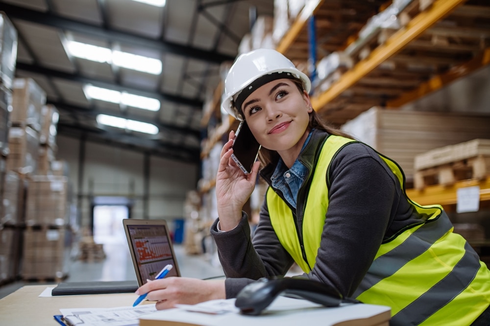 warehouse worker on a cell phone at a desk with a laptop and scanner