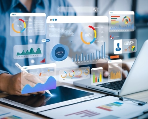 person on a laptop and tablet with icons floating in the showing what they are working on different charts and graphs