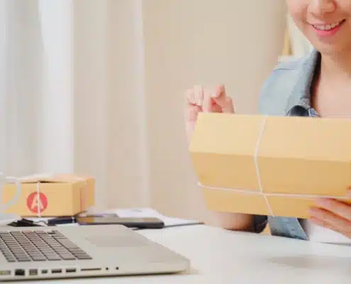 Woman managing warehouse shipments with laptop and packages for WMS inventory control