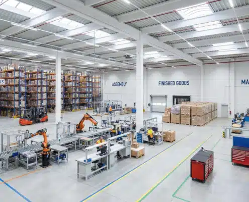 Wide warehouse interior segmented into zones for materials, assembly, finished goods, and maintenance tools.
