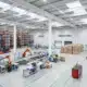 Wide warehouse interior segmented into zones for materials, assembly, finished goods, and maintenance tools.