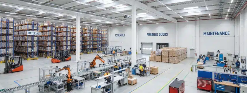 Wide warehouse interior segmented into zones for materials, assembly, finished goods, and maintenance tools.
