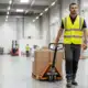 Warehouse worker in safety vest pulling pallet jack through distribution center