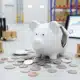 Broken white piggy bank with scattered coins representing budget-conscious warehouse efficiency solutions