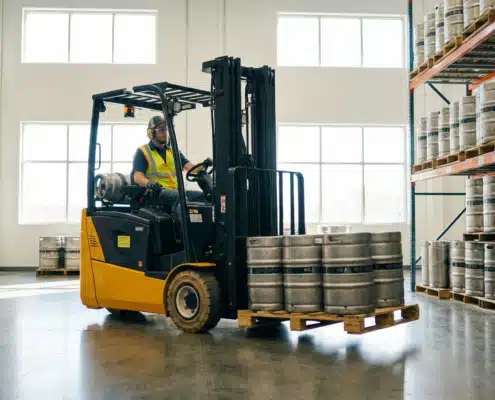 Warehouse worker operating yellow forklift transporting beer kegs in beverage distribution facility
