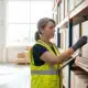 Warehouse worker in safety vest organizing inventory with clipboard and labels