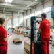 Two warehouse workers in red uniforms collaborating on inventory management in modern facility