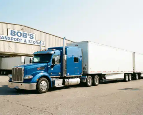 Blue semi-truck with white trailers parked outside Bob's Transport and Storage warehouse facility