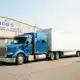Blue semi-truck with white trailers parked outside Bob's Transport and Storage warehouse facility