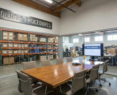 Modern warehouse conference room with Policy & Procedures sign and inventory shelves