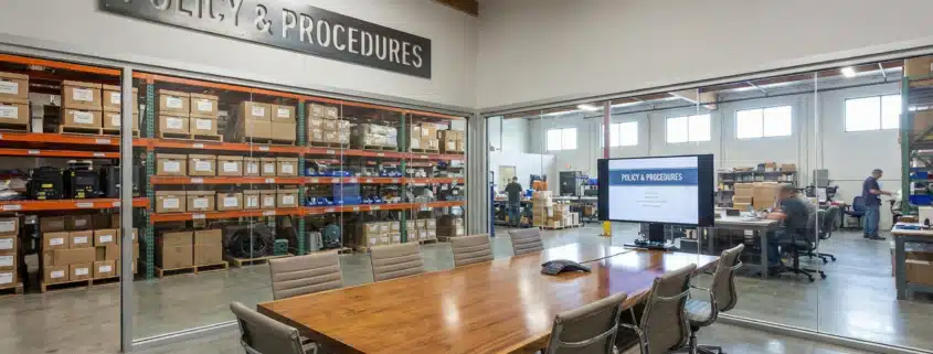 Modern warehouse conference room with Policy & Procedures sign and inventory shelves